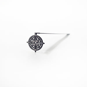 Black metal compass rose bookmark standing on white surface with long diagonal shadow — isolated product photo