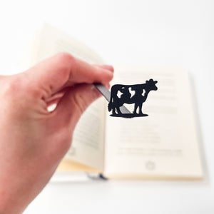 Hand holding cow silhouette bookmark close-up with open book blurred in background