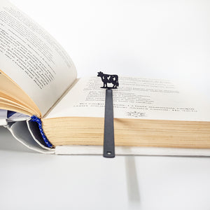 Black steel cow bookmark clipped to page corner, 0.6 mm blade visible from edge