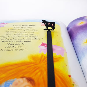 Cow silhouette metal bookmark detail against illustrated book page with pink and yellow tones