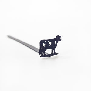 Black steel cow bookmark resting on closed book, product detail on neutral background