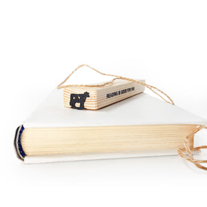 Metal cow bookmark on wooden gift block stamped READING IS GOOD FOR YOU, white background