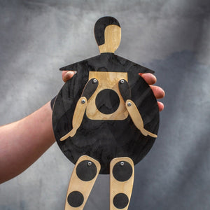 Close-up of the Bauhaus Beetle puppet held in hands — round black plywood body with riveted jointed arms and dotted legs