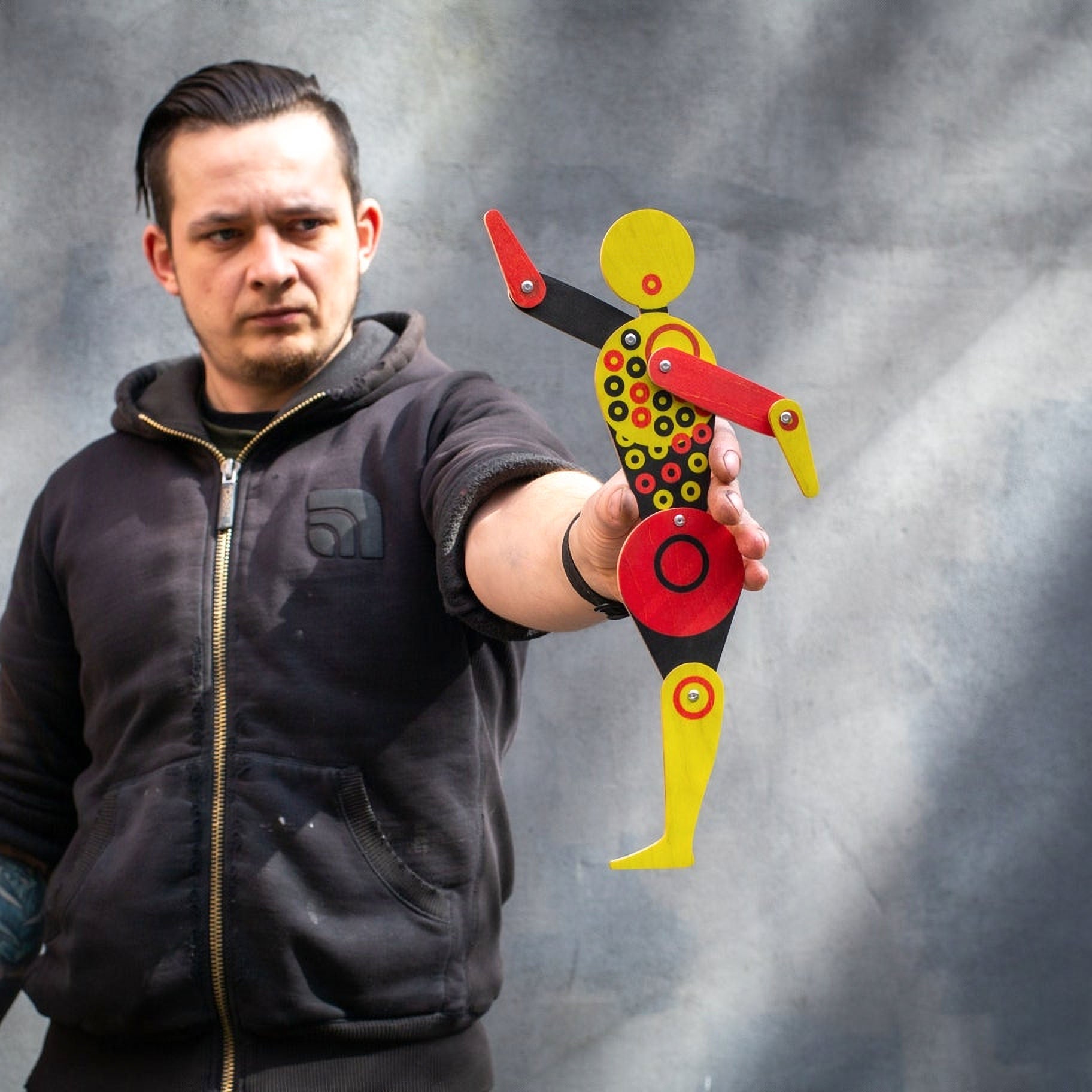 Maker holding Bauhaus circle dancer puppet at arm's length showing scale against grey background