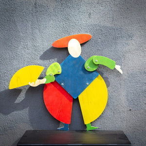 Bauhaus harlequin wooden puppet displayed on textured grey wall, arms posed outward