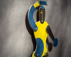 Side angle of blue and yellow Bauhaus puppet mounted on textured wall