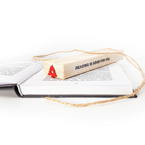 Red bonfire metal bookmark displayed with wooden block engraved Reading is good for you resting on open book, eco friendly gift packaging