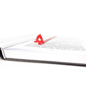 Close up of red bonfire metal bookmark placed inside open book, minimalist steel flame page marker on white pages
