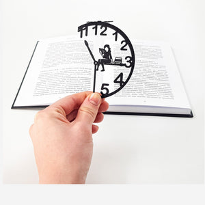 Book O’Clock metal bookmark held in a hand above an open book