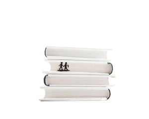 Black metal bookmark shaped like two children holding hands and walking with a lantern, inserted between the pages of a stacked white book, titled “Into Adventure.” Designed and made in Ukraine. Not mass-produced.