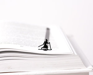 Skier in High Hat metal bookmark marking a page in an open book