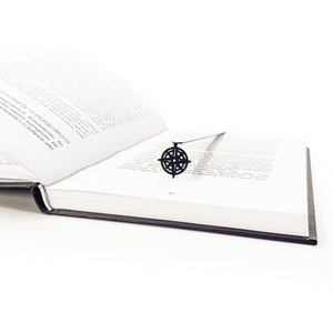 Metal bookmark with compass rose pendant in open dark-bound book, diagonal angle view
