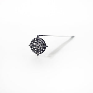 Black metal compass rose bookmark standing on white surface with long diagonal shadow — isolated product photo