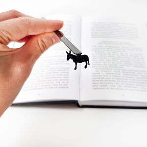Slim black donkey bookmark resting on open book pages, angled overhead view