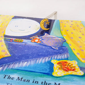 Gold moon and star bookmark clipped to the top of a colorful children’s book illustration showing a smiling moon and cozy bedroom scene