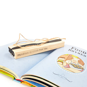 Knife-shaped COOK bookmark placed in a wooden gift block engraved with “Reading is good for you,” resting on an open children’s cookbook page titled “Food Rhymes.”
