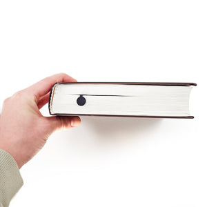 Side view of a book showing the thin black metal lady golf player bookmark inside the pages, demonstrating its slim profile