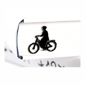 Lady on the Bike metal bookmark resting on the pages of an open book