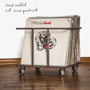 Hand-welded black metal record crate with wheels, filled with vinyl records, featuring handwritten notes about custom orders and non-mass production.