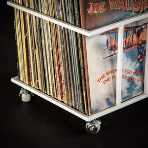 Close-up of white metal vinyl record crate on wheels, filled with vintage LPs, highlighting durable welded frame and smooth caster wheels.
