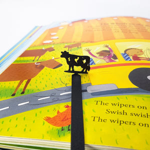Metal cow bookmark standing above farm scene in colorful children's storybook