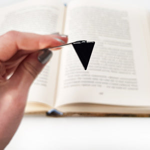 Minimalist Triangle metal bookmark held in a hand above an open book