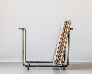 Side view of a minimalist vinyl record rack made from raw steel, showing LP records neatly stored in an open rectangular frame with upright supports.