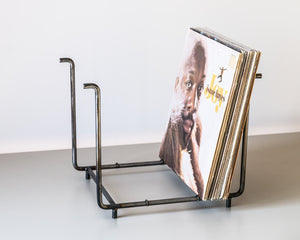 Angled side view of a handcrafted raw steel LP record rack holding a stack of vinyl albums, including “Joy” by Isaac Hayes, on a neutral surface.