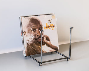 Angled view of a raw steel vinyl record rack with an open rectangular frame, holding the LP “Joy” by Isaac Hayes, placed on a light grey surface.