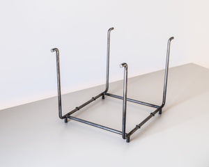 Angled top-down view of an empty minimalist vinyl record rack made of hand-welded raw steel, featuring an open frame with four upright supports.