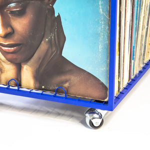 Close-up of a blue metal vinyl record cart with wheels, showing a vintage record cover featuring a woman’s face and a neat row of albums stored upright.