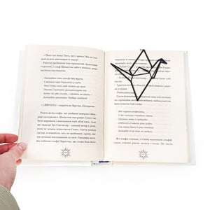 Black metal origami bird bookmark placed inside an open book, marking the page with a clean geometric silhouette.