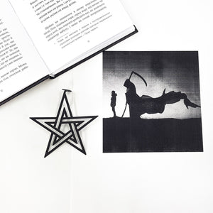 Black star-shaped bookmark and silhouette of a person with a scythe on a white surface.