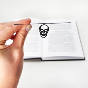 Hand holding a black metal skull bookmark on a white background