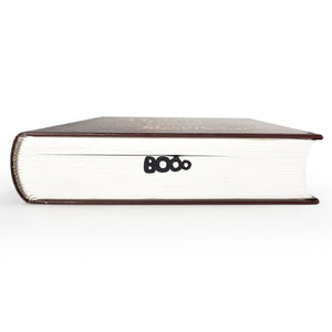 Close-up of a thick book with a black metal bookmark peeking out, shaped like the word “BOO” in playful ghostly letters.