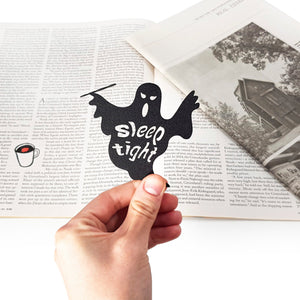 Black ghost-shaped bookmark with 'Sleep tight' text held over an open book.