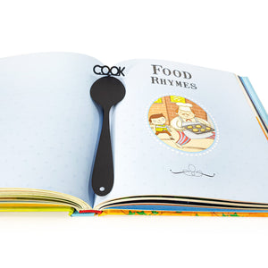 Black metal spoon-shaped bookmark with the word “COOK” placed inside an open children’s book titled Food Rhymes, with colorful illustrations.