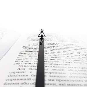 black teepee-shaped metal bookmark lying across an open book with Cyrillic text, tip pointing toward the top of the page.