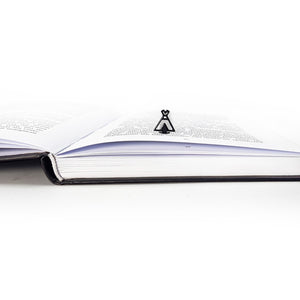Side view of an open book with a black teepee-shaped metal bookmark standing upright between the pages.