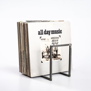 Minimalist metal vinyl record stand in transparent finish holding a large collection of LPs, displayed on white background.
