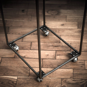 Close-up of industrial-style metal frame with ball casters, showing welded joints and wood floor background.
