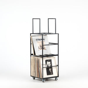 Minimalist black metal vinyl record holder on wheels, displaying LPs with two open compartments and vertical bars. Functional, sleek design ideal for modern interiors.