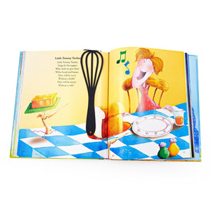 A black whisk-shaped metal bookmark lies across the left page of an open children’s book featuring the rhyme “Little Tommy Tucker” with colorful illustrations of bread, butter, and a singing child.