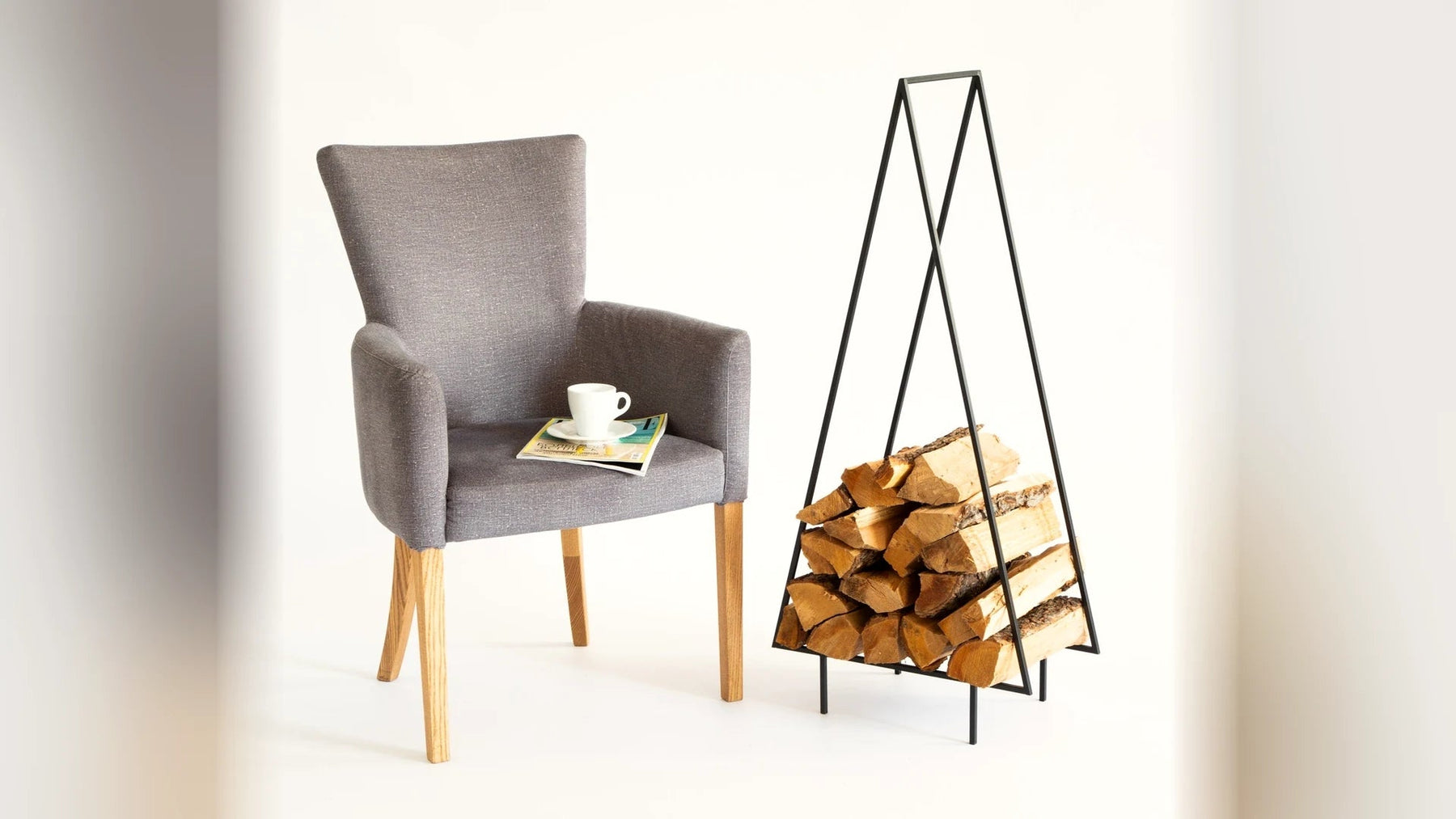 Armchair beside a black steel log holder stacked with firewood.