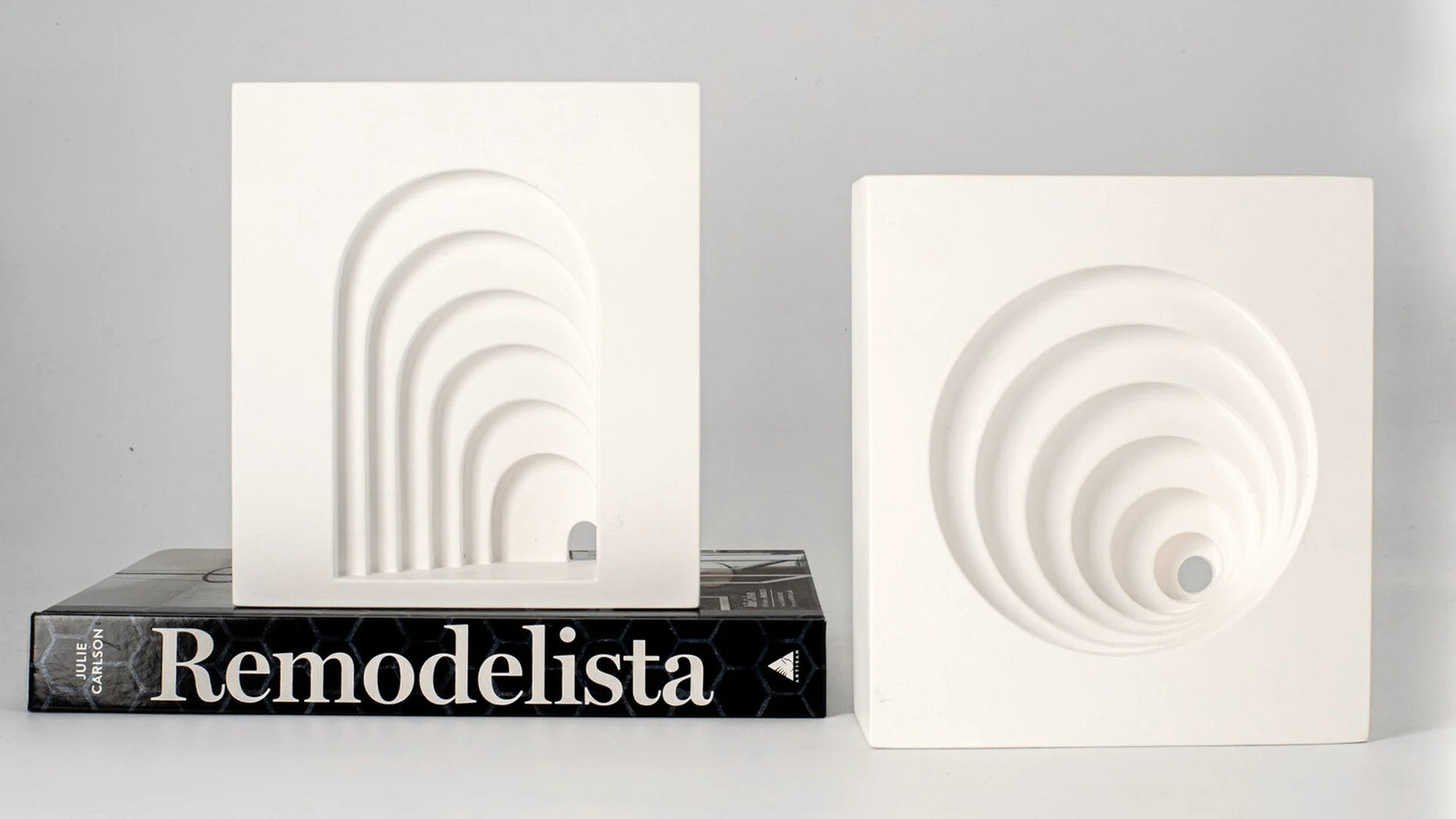 Architectural plaster bookends framing a design book on a shelf.
