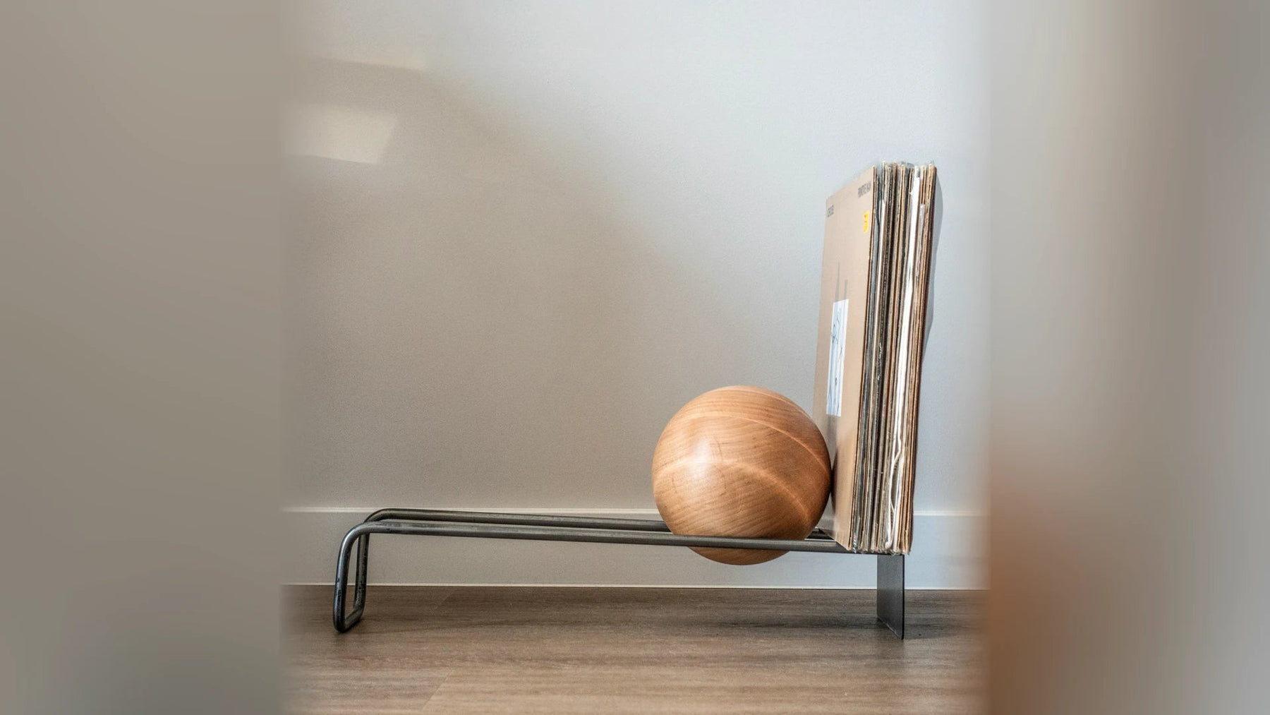 Side view of a low steel record stand with a wooden ball, holding LPs.