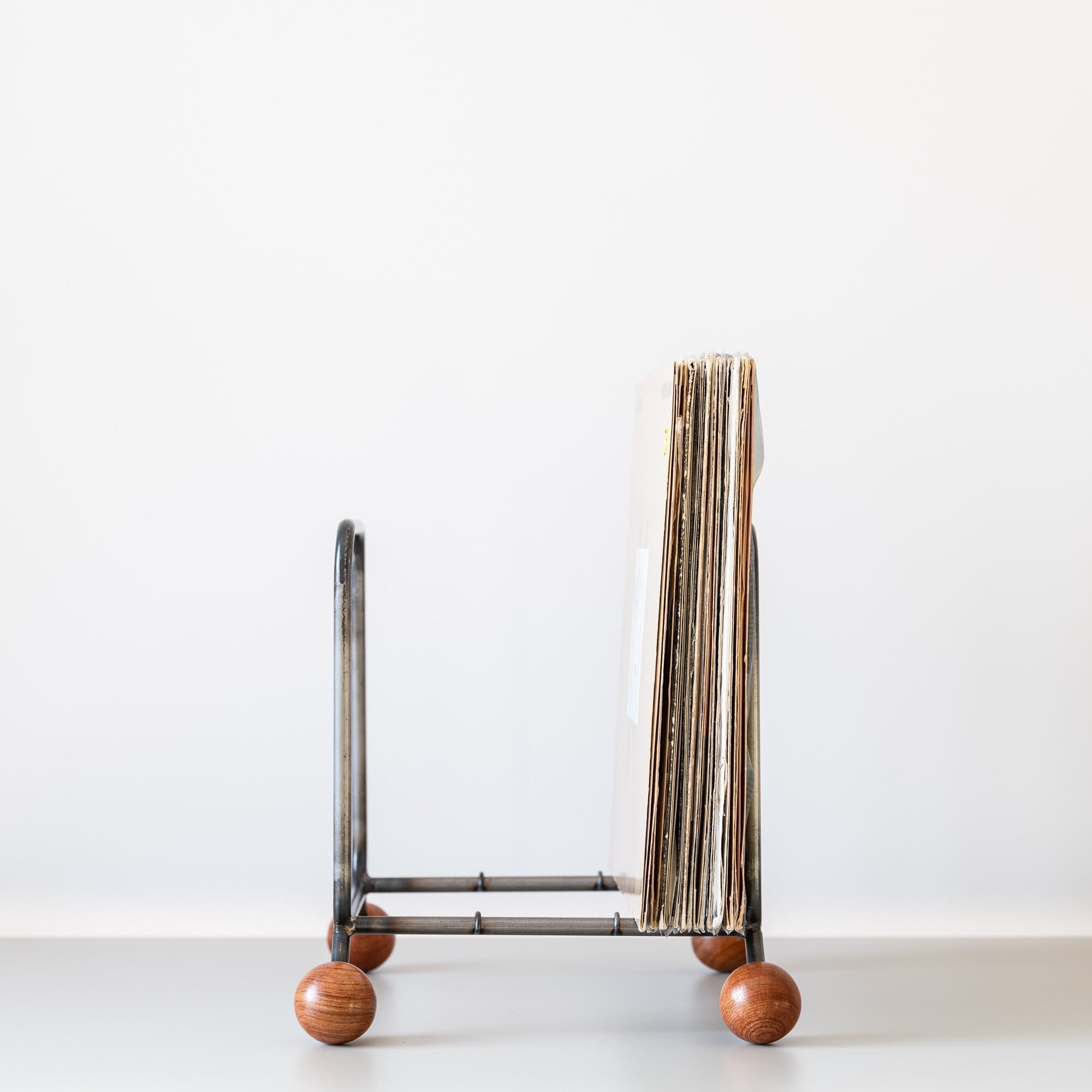 Minimalist steel vinyl record rack with wooden ball feet, holding LP records
