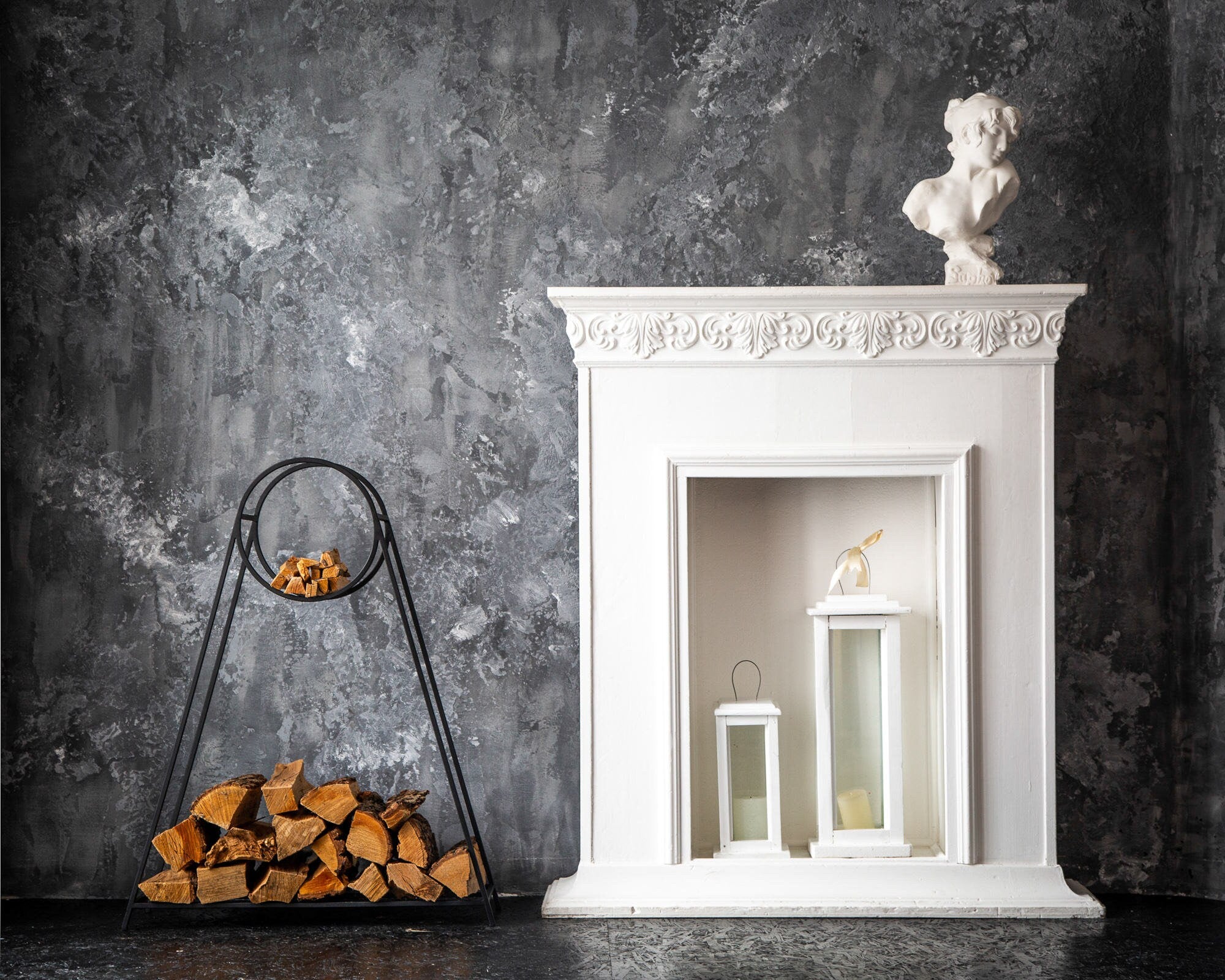 Black metal log holder with firewood beside a white decorative fireplace — indoor firewood storage in a styled living room