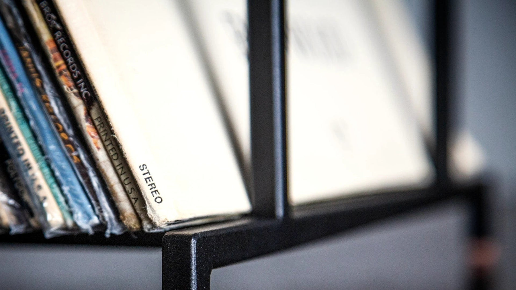 Close-up of LP record sleeves in a steel stand in low light.