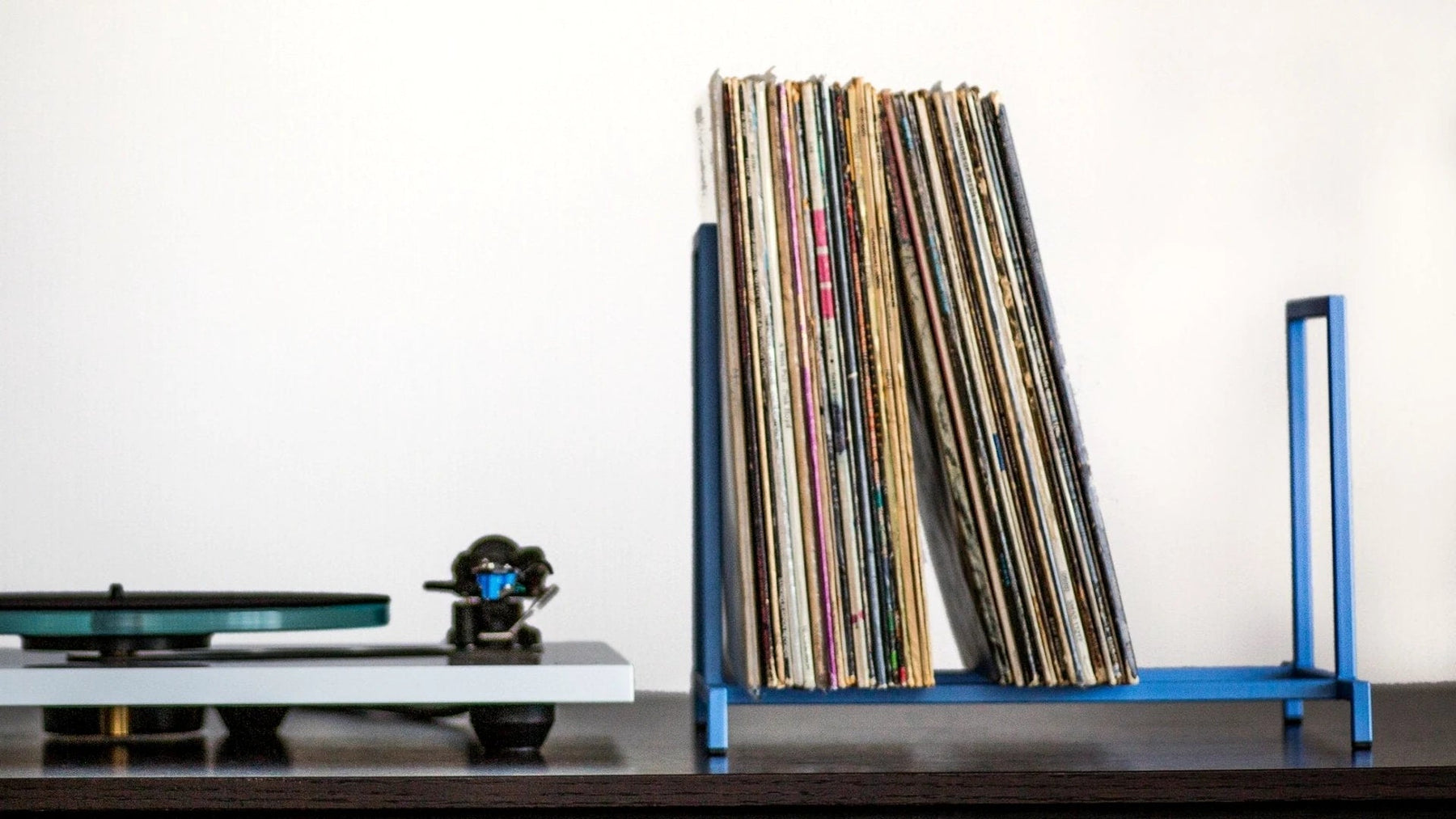LP records filed upright in a blue steel stand beside a turntable.